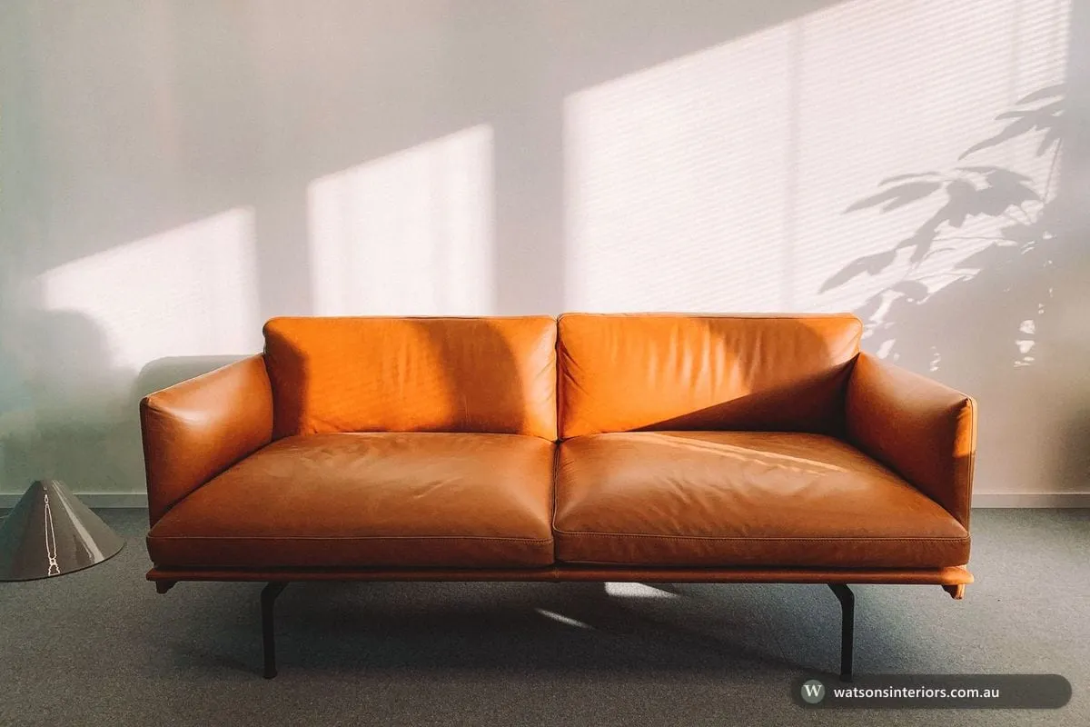 A tan leather two-seater sofa with slim metal legs on a clean light background